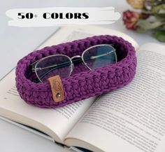 an open book with glasses on it next to a purple crochet bracelet and sunglasses case