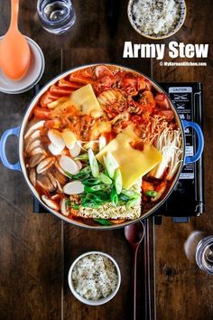 a large pot filled with lots of food on top of a wooden table next to bowls and utensils