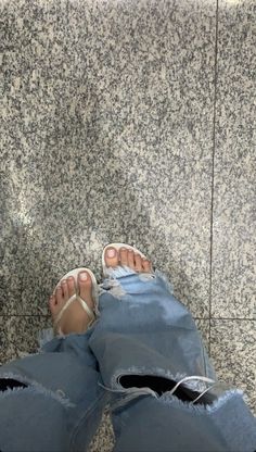 a person with their feet propped up in ripped jeans and white sandals, sitting on a tile floor