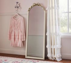 a large mirror sitting next to a window in a room with pink walls and curtains