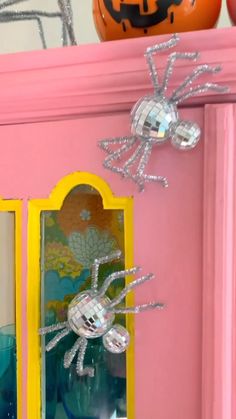 an orange pumpkin sitting on top of a pink shelf next to a glass vase with a spider in it