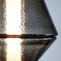 a shiny glass vase sitting on top of a reflective tableclothed surface with light reflecting off it's side