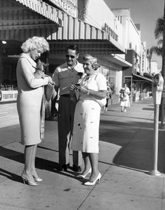 an old black and white photo of three people on the sidewalk talking to each other