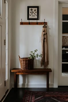 a wooden bench sitting in front of a white wall next to a doorway with a potted plant on top of it