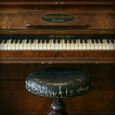 an old piano sitting on top of a wooden floor next to a stool with a black leather seat