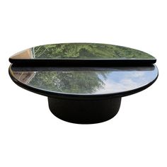 an oval glass table top with trees in the back ground and sky reflected on it