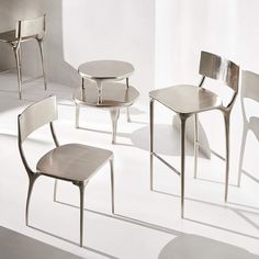 four chairs and one table are arranged in a white room with shadows on the floor