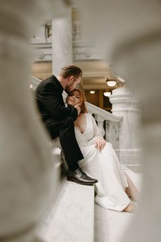 a man and woman are sitting on the stairs in their wedding attire looking at each other