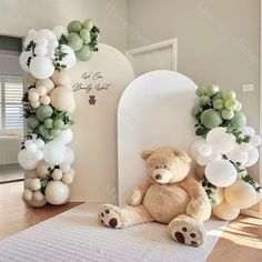 a teddy bear sitting on the floor next to balloons and greenery in front of it