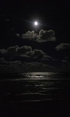 the moon is shining brightly over the ocean at night with dark clouds and water below