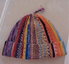 a multicolored knitted hat laying on top of a piece of cloth next to a mirror