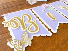 a purple and gold birthday banner with butterflies on it's side, next to a wooden table