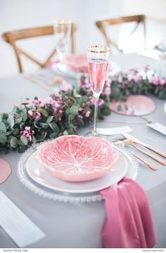 the table is set with pink plates, silverware and greenery for an elegant touch