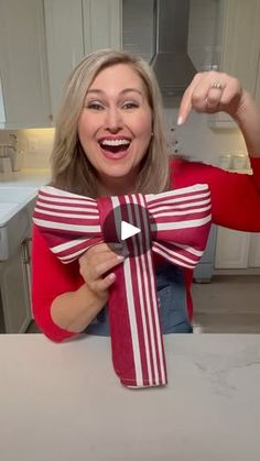 a woman holding up a red and white striped gift wrapped in paper with a bow