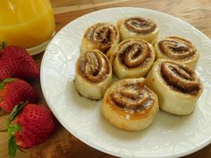 some cinnamon rolls on a white plate with strawberries and orange juice in the background