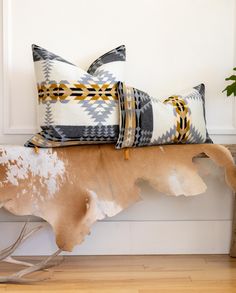 two decorative pillows sitting on top of a wooden bench next to a potted plant