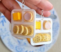 a person is holding a miniature lunch box with crackers and cheeses in it