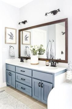 a bathroom with blue cabinets and white counter tops, two mirrors above the sink and flowers in vases