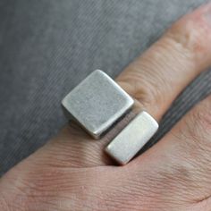 a person's hand wearing a silver ring with two squares on the middle of it