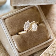 an engagement ring with two pear shaped diamonds in a velvet box on a carpeted surface