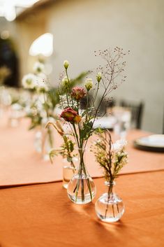 two vases with flowers are sitting on a table in front of plates and napkins