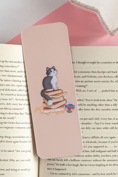 a bookmark with a cat sitting on top of a stack of books next to an open book