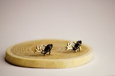 two small black and gold earrings sitting on top of a wooden stand