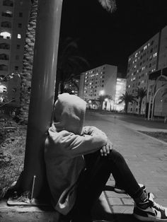 a person sitting on a bench in front of a pole at night with their head turned to the side