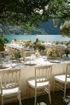 an outdoor table set up with white chairs and flowers in vases on the tables