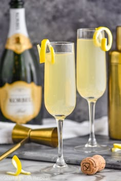 two champagne flutes with lemon wedges next to bottles