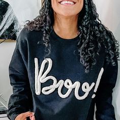 a woman wearing a black sweatshirt with the word boo spelled on it in white letters