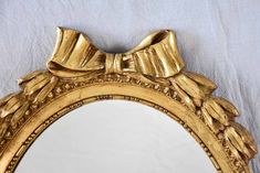 a gold framed mirror with a bow on the top and bottom edge, hanging on a wall