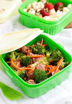 two green plastic containers filled with food on top of a white cloth next to utensils