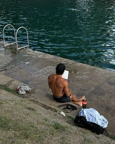 a man sitting on the edge of a body of water next to a swimming pool