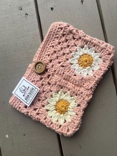 a crocheted pink and white flowered blanket with buttons on the front, sitting on a wooden surface