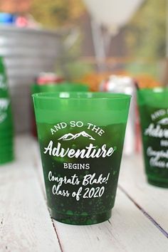 green cups with white lettering on them sitting on a wooden table next to other plastic cups