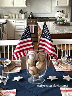 an american flag and baseballs in a glass vase on a table with wine glasses