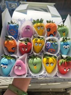 a box filled with lots of different colored chocolate covered strawberries next to a person's hand