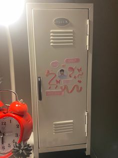 an orange alarm clock sitting next to a locker with stickers on it and the door open