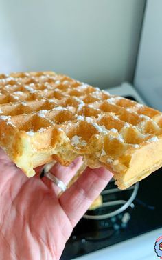 a hand holding up a waffle on top of a stove