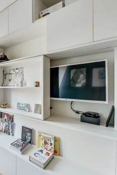 a flat screen tv sitting on top of a white shelf next to a book case