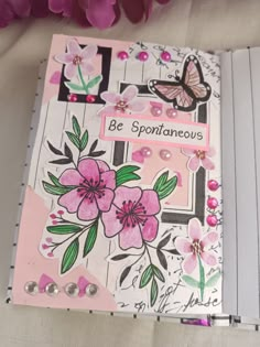 an open notebook with pink flowers and butterflies on the cover, sitting on a table