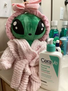 a green alien stuffed animal sitting on top of a bathroom sink next to a bottle of lotion