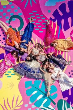 a group of women standing on top of each other in front of a colorful wall