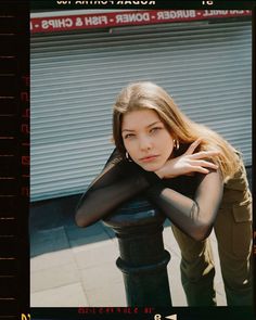 a woman leaning on a pole in front of a building