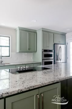 a kitchen with green cabinets and white marble counter tops, stainless steel appliances and an oven