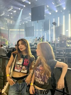 two young women standing next to each other in front of a stage with lots of lights