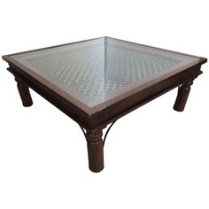 a glass top coffee table with wooden legs and an intricate design on the bottom surface