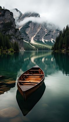 a small boat floating on top of a lake next to a mountain covered in clouds