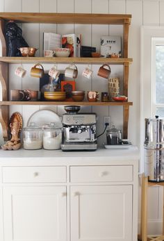 a kitchen with white cupboards and shelves filled with coffee pots, pans and other items